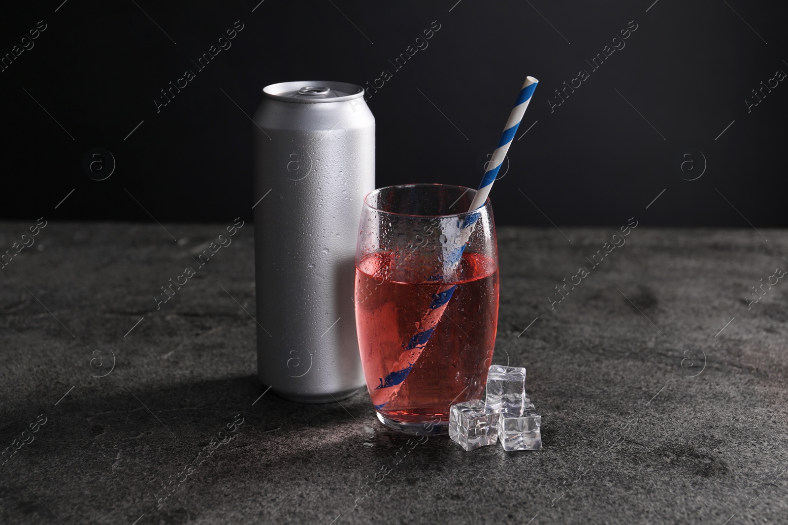 Photo of Energy drink in glass, aluminium can and ice cubes on grey table