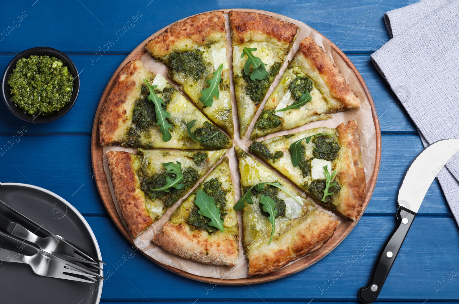 Photo of Delicious pizza with pesto, cheese and arugula served on blue wooden table, flat lay