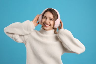 Photo of Happy woman wearing warm earmuffs on light blue background