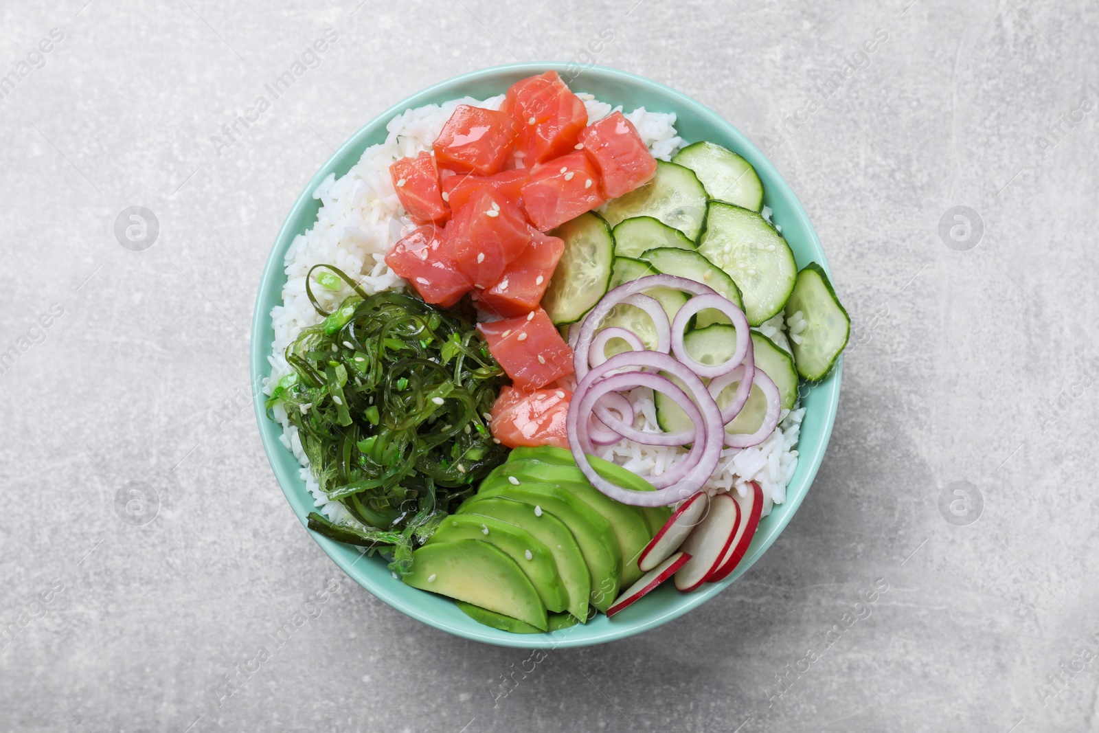 Photo of Delicious poke bowl with salmon, seaweed and vegetables on light grey table, top view