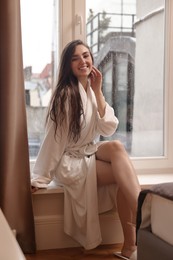 Photo of Young woman wearing bathrobe with beautiful washed hair sitting on windowsill in shower at home