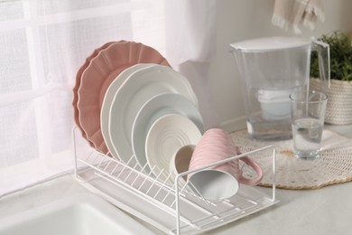 Photo of Drainer with different clean dishware and cup on light table indoors