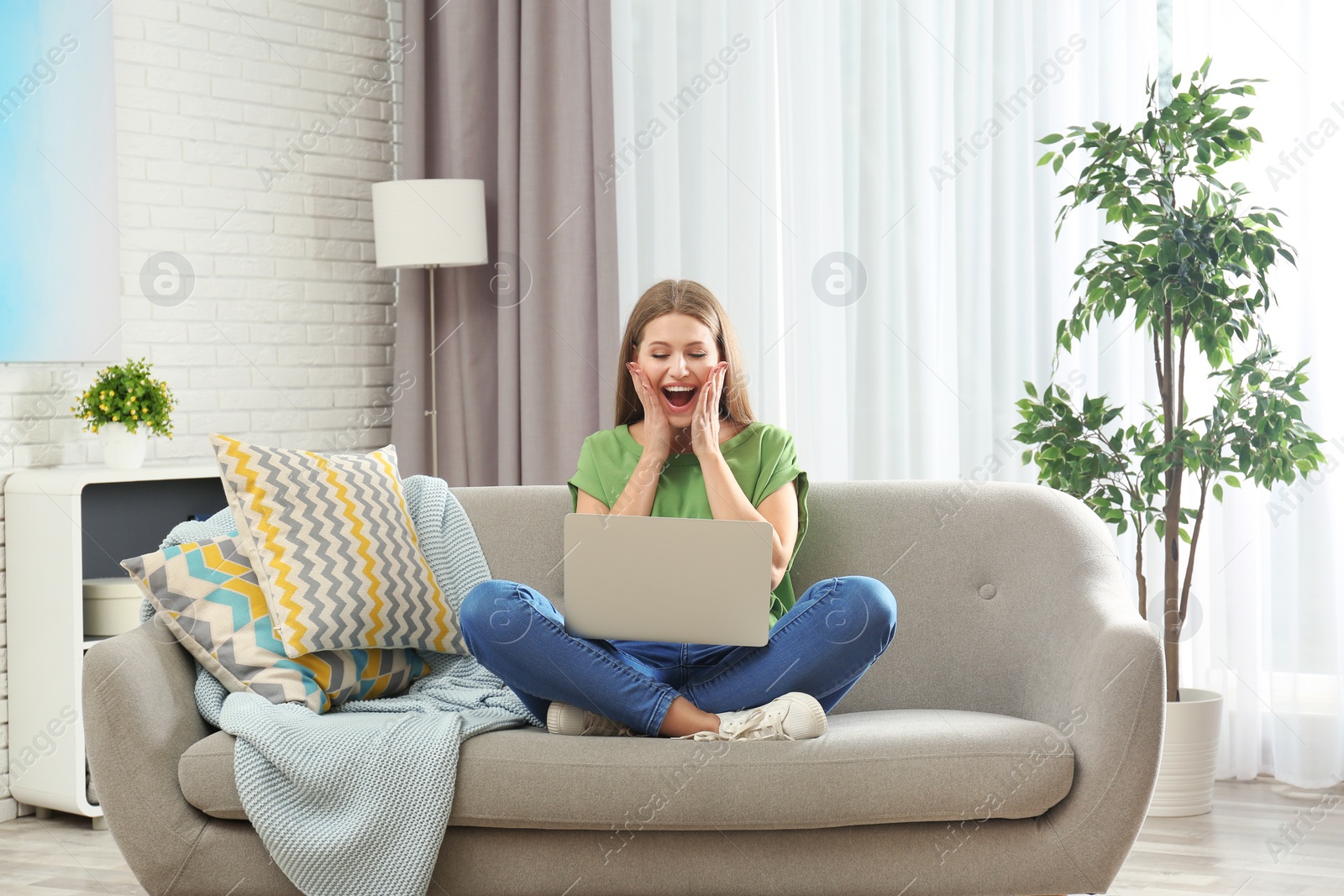 Photo of Emotional young woman with laptop celebrating victory on sofa at home