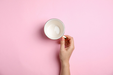 Woman with empty cup on light pink background, top view