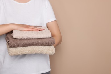 Woman holding folded soft terry towels on light brown background, closeup. Space for text
