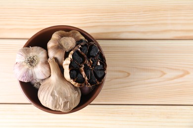 Fermented black garlic in bowl on wooden table, top view. Space for text