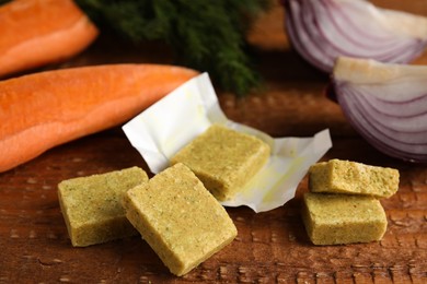 Bouillon cubes and other ingredients for soup on wooden table, closeup