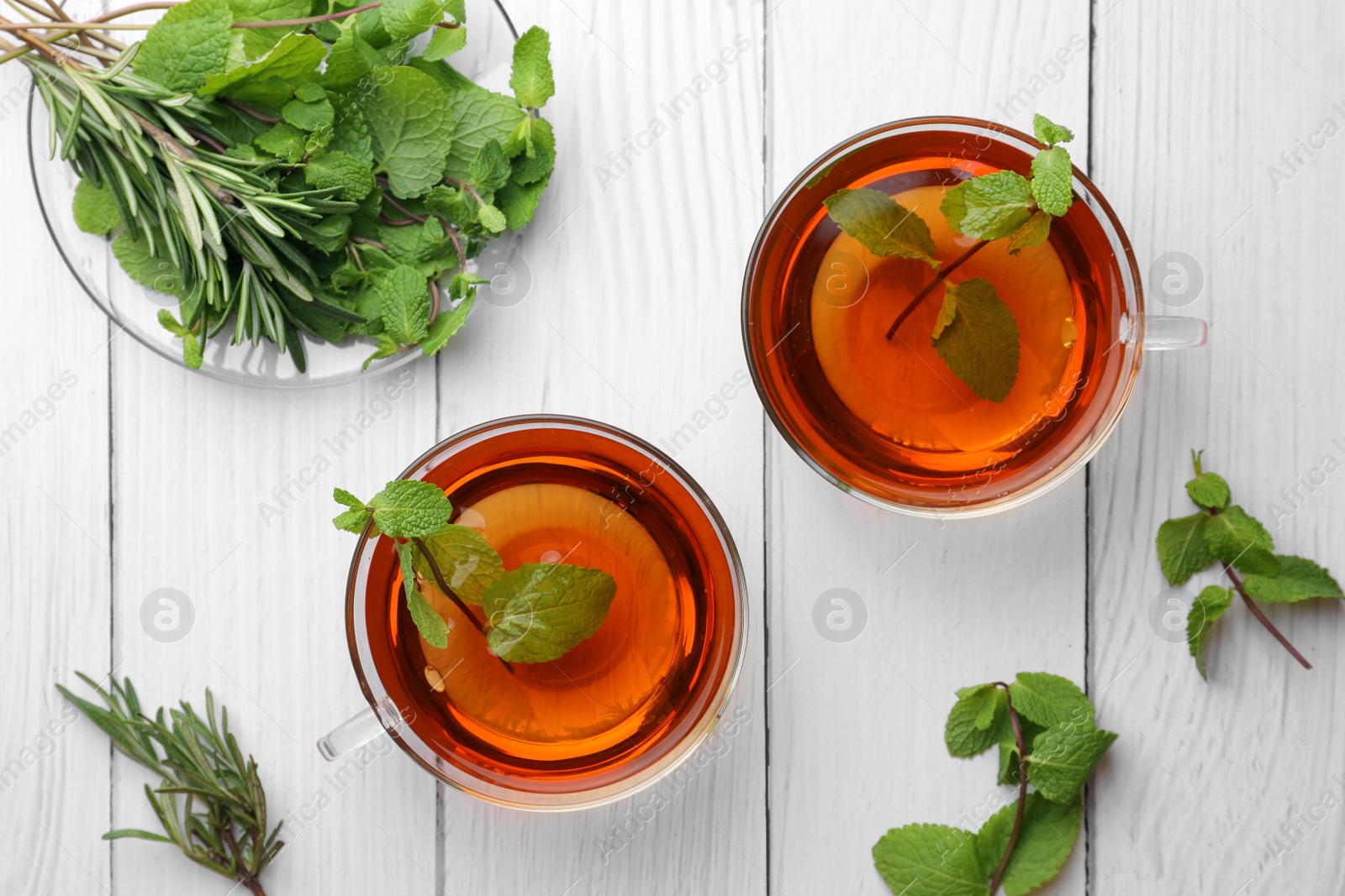 Photo of Cups of aromatic herbal tea with mint and rosemary on white wooden table, flat lay