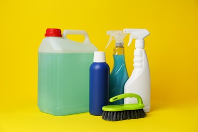 Photo of Bottles of detergents and brush on yellow background. Cleaning supplies