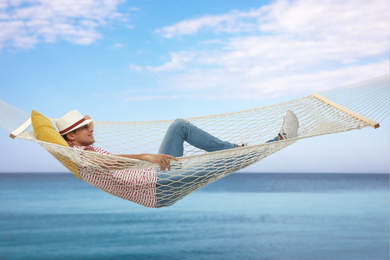 Man resting in hammock near sea on sunny day 