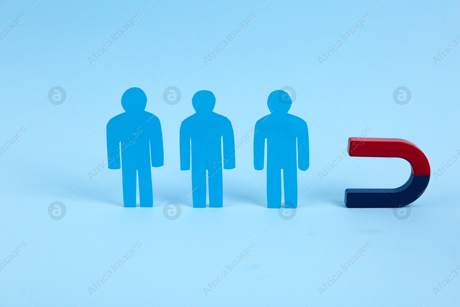 Photo of Magnet attracting paper people on light blue background