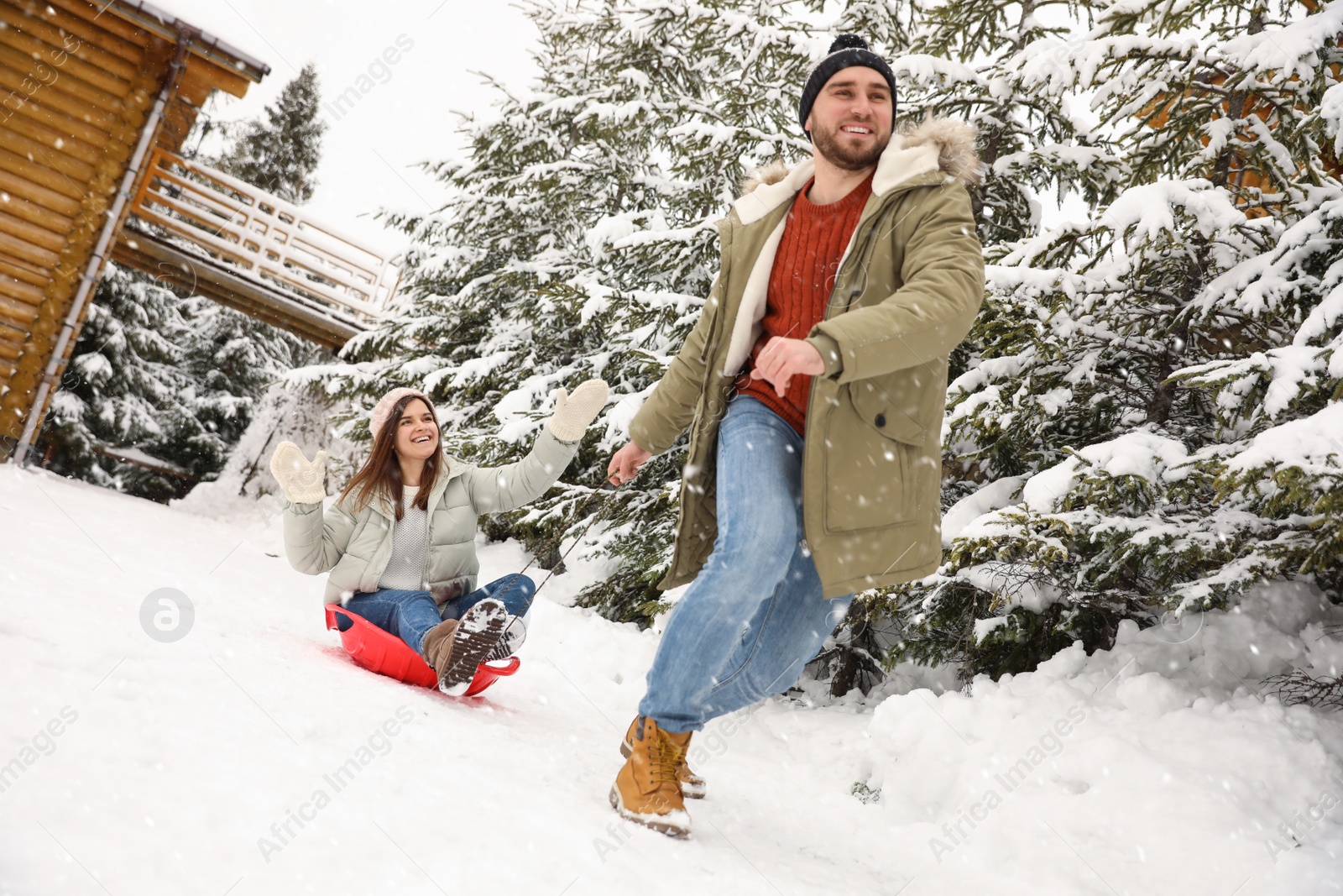 Photo of Young man pulling sled with his girlfriend outdoors on snowy day. Winter vacation