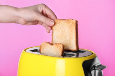 Woman taking roasted bread out of toaster on pink background, closeup