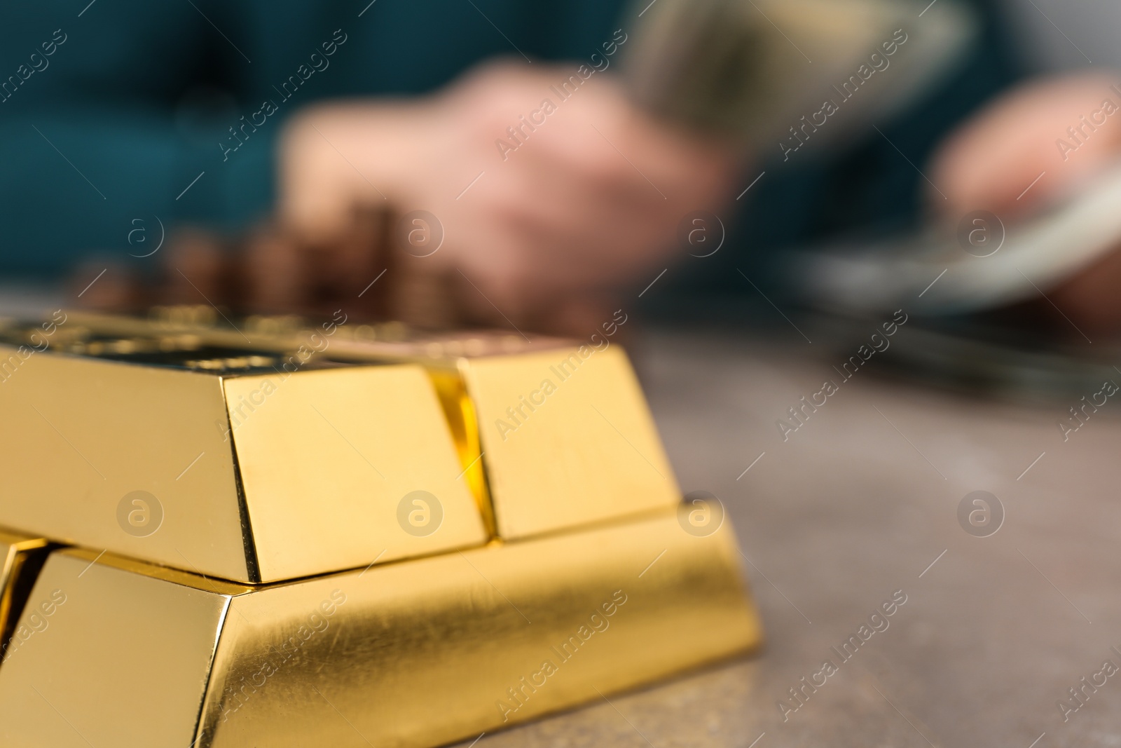 Photo of Stacked gold bars and man counting money at table, closeup. Space for text