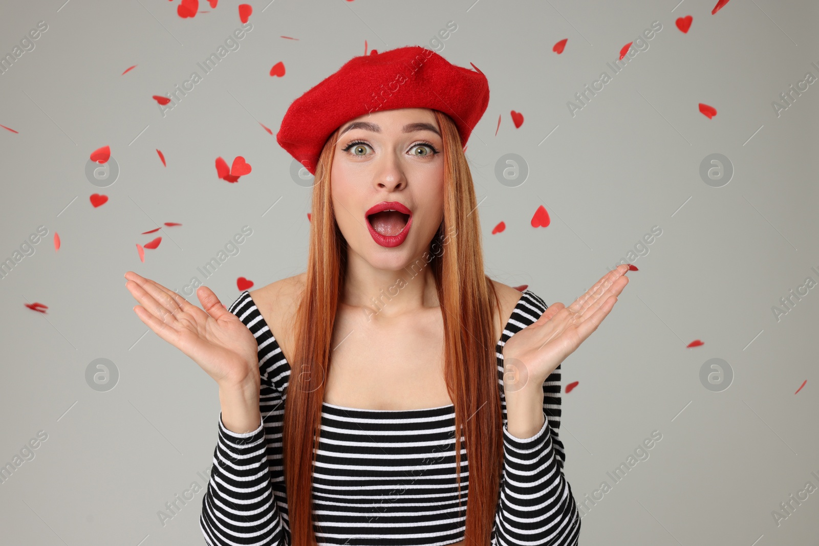 Photo of Emotional young woman under heart shaped confetti on light grey background