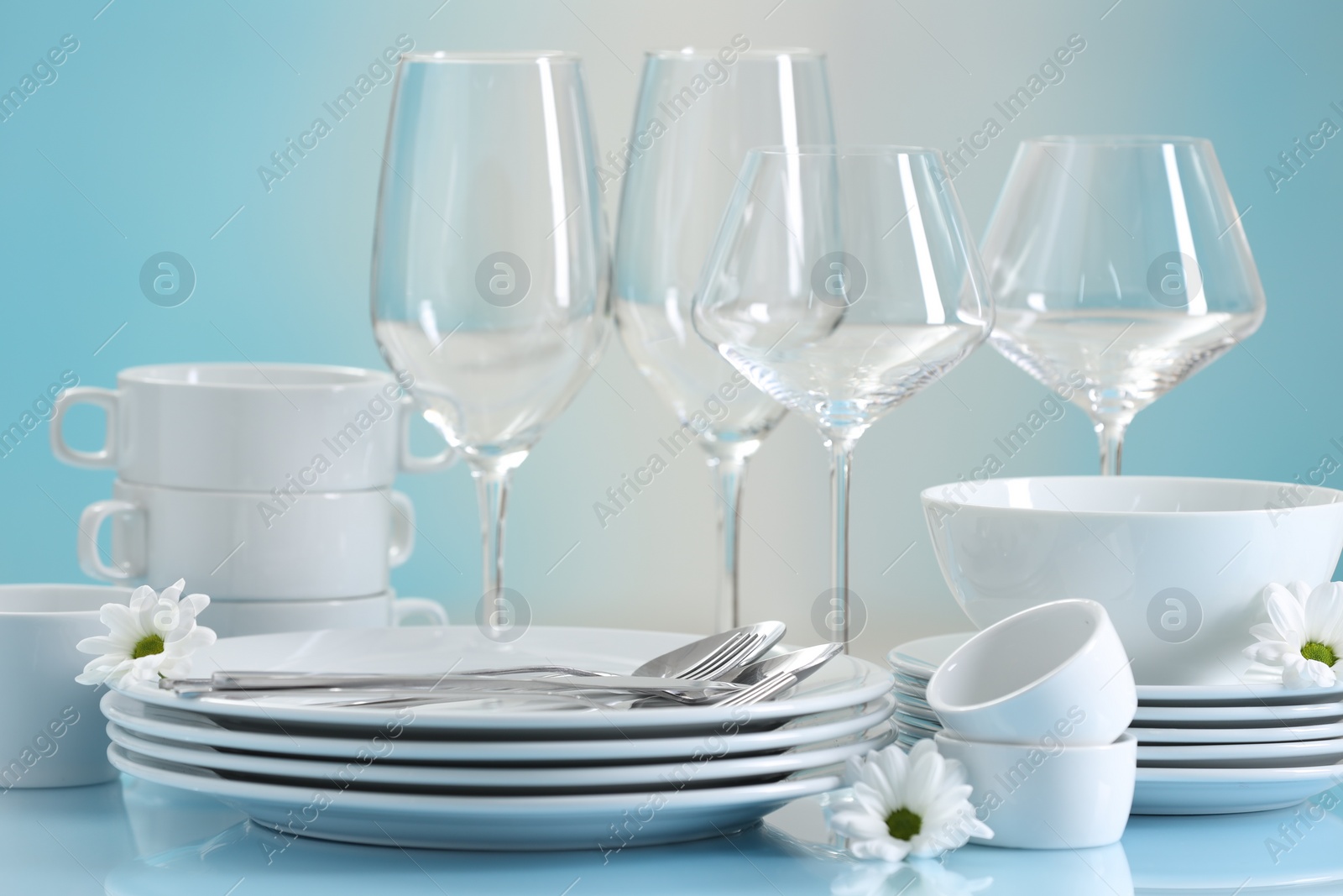 Photo of Set of many clean dishware, cutlery, flowers and glasses on light blue table