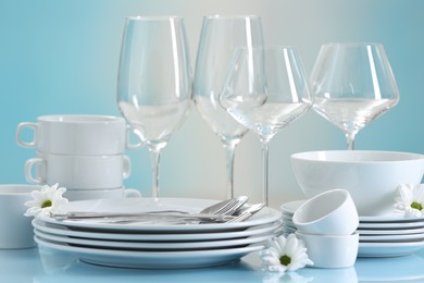 Photo of Set of many clean dishware, cutlery, flowers and glasses on light blue table