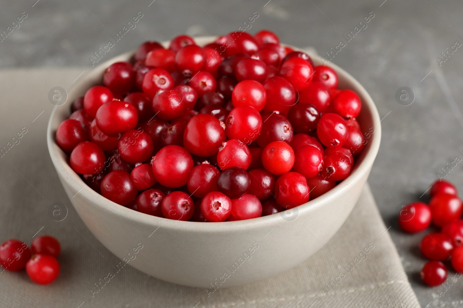 Photo of Cranberries in bowl on light grey table, closeup