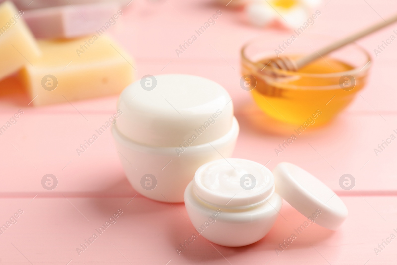Photo of Jars of cream with natural beeswax component on pink wooden table, closeup