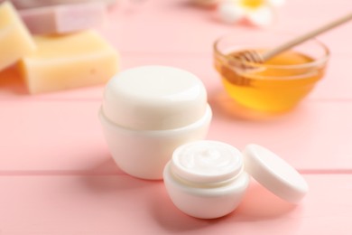 Photo of Jars of cream with natural beeswax component on pink wooden table, closeup