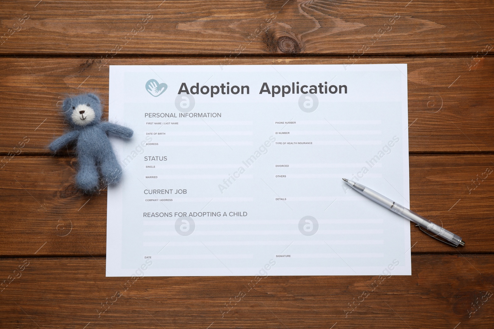 Photo of Adoption application, toy bear and pen on wooden table, flat lay