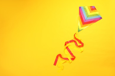 Photo of Bright rainbow kite on yellow background, top view. Space for text