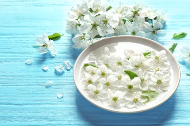 Photo of Bowl with water and blossoming flowers on wooden background