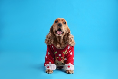 Photo of Adorable Cocker Spaniel in Christmas sweater on light blue background