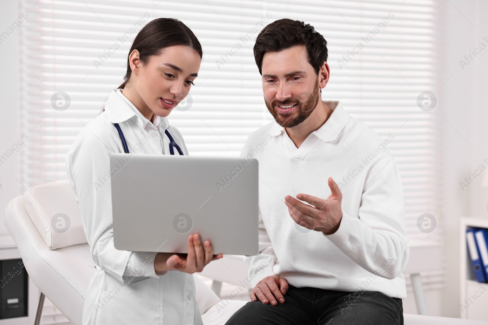 Photo of Doctor with laptop consulting patient during appointment in clinic