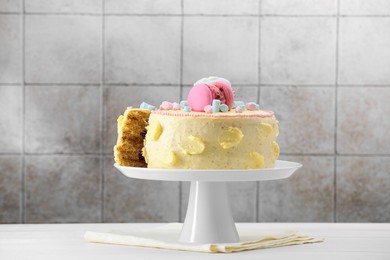 Photo of Delicious cake decorated with macarons and marshmallows on white wooden table against tiled background
