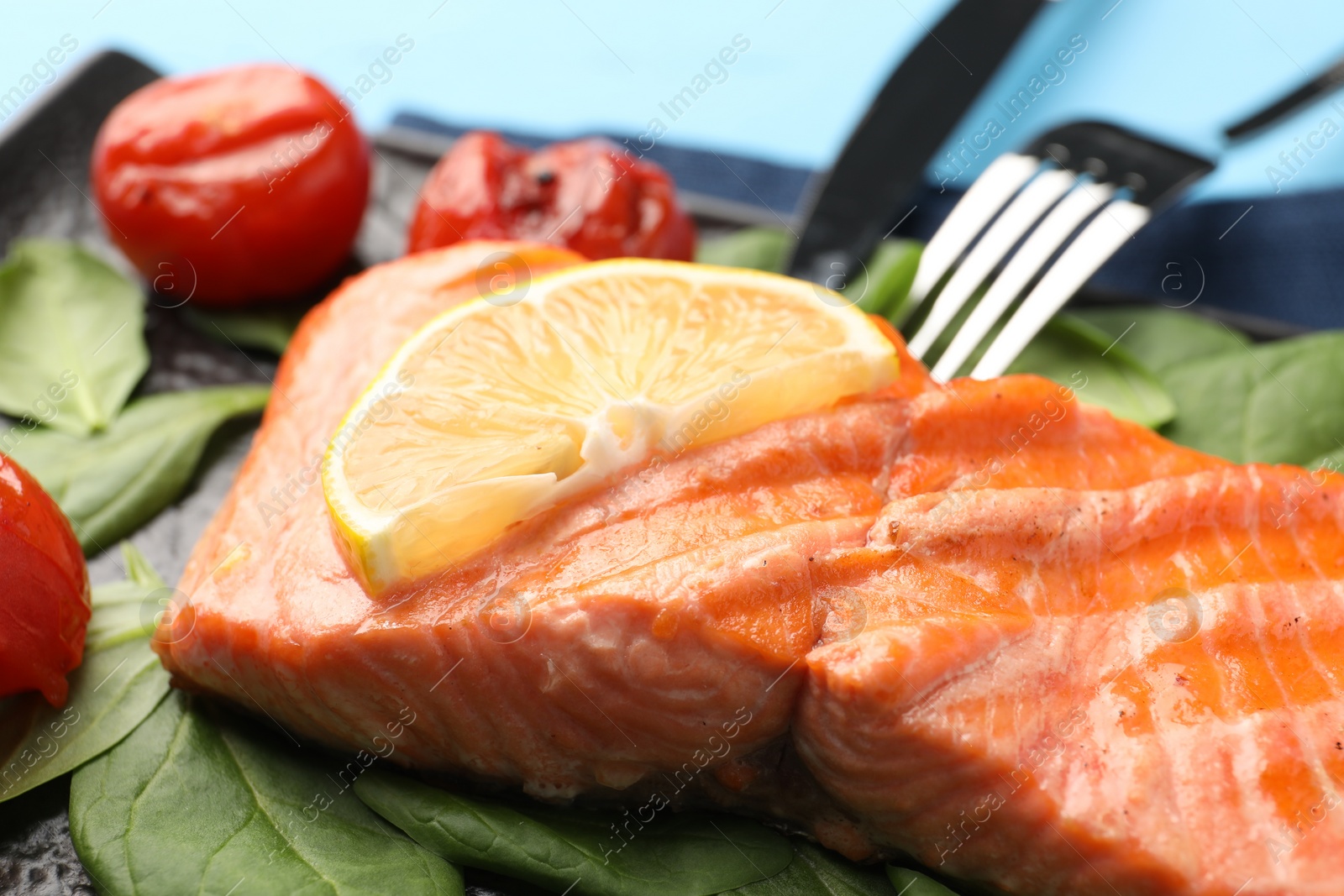 Photo of Tasty grilled salmon with tomatoes, spinach and lemon on table, closeup