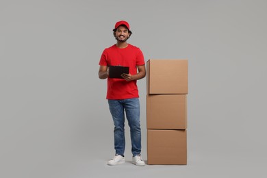 Photo of Happy courier with clipboard and stack of parcels on grey background