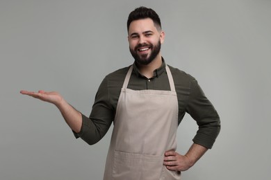 Smiling man in kitchen apron holding something on grey background. Mockup for design