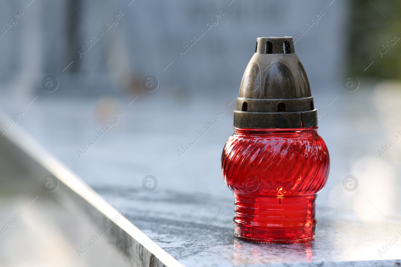 Photo of Red grave lantern with burning candle on granite tombstone outdoors, space for text