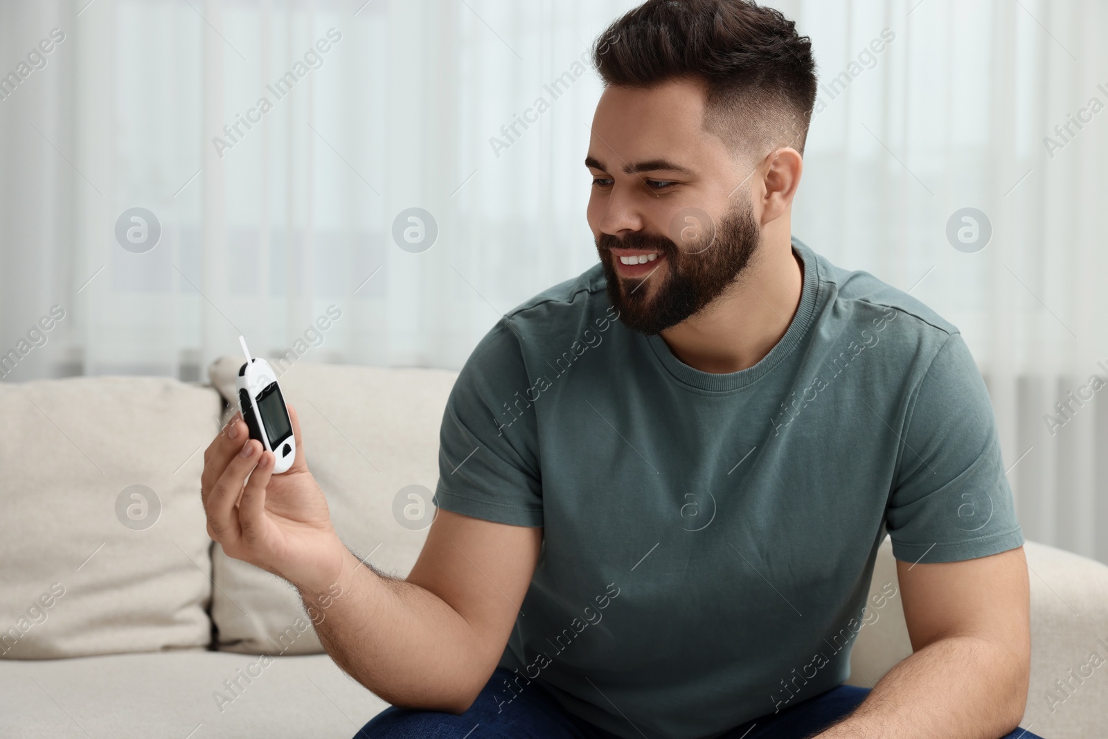 Photo of Diabetes test. Smiling man with glucometer at home