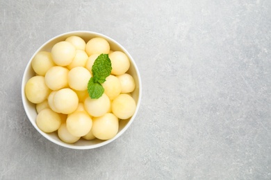 Photo of Melon balls and mint in bowl on light grey table, top view. Space for text