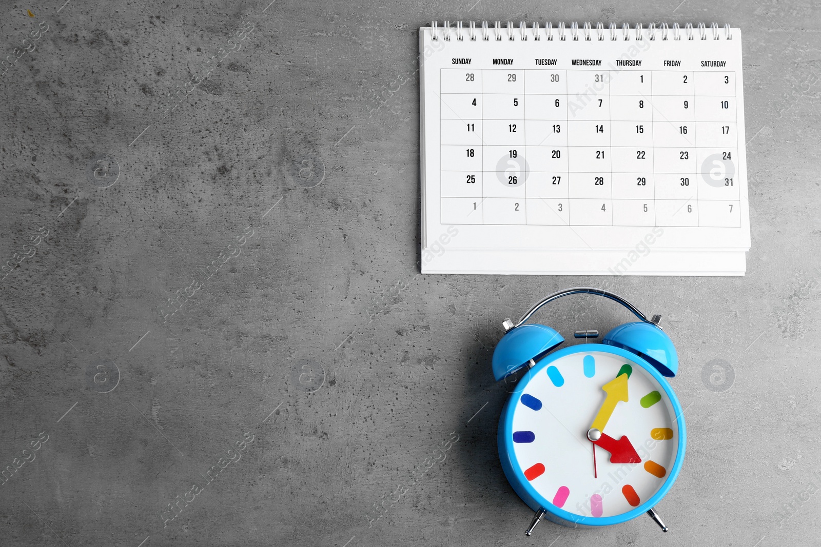 Photo of Calendar and alarm clock on grey stone background, flat lay. Space for text