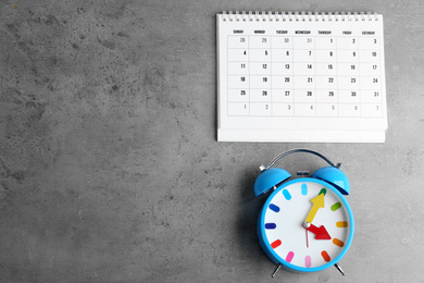 Photo of Calendar and alarm clock on grey stone background, flat lay. Space for text