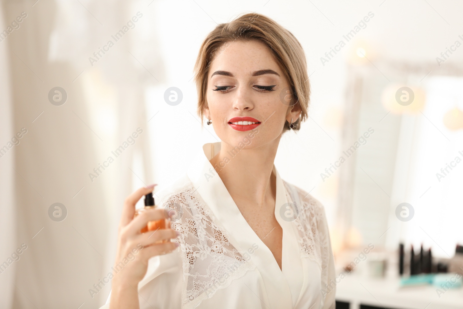 Photo of Beautiful young bride holding bottle of perfume indoors. Wedding preparation