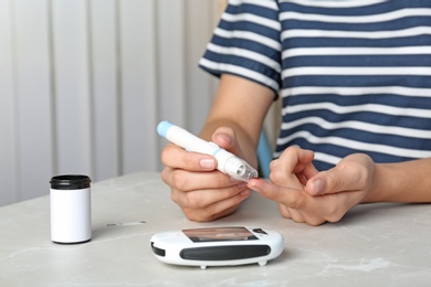 Photo of Woman using lancet pen at table. Diabetes test