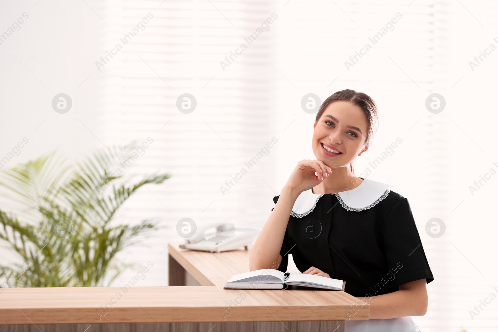 Photo of Young chambermaid near reception in hotel. Space for text