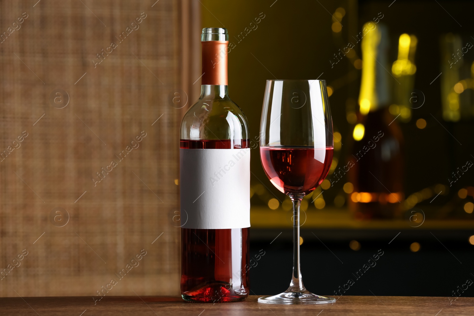 Photo of Bottle and glass of delicious rose wine on wooden table in bar