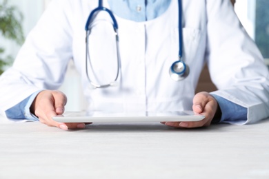 Photo of Female doctor with modern tablet sitting at table indoors, closeup