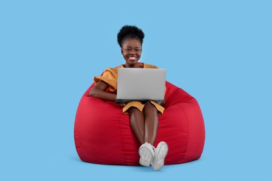 Photo of Beautiful young woman with laptop sitting on beanbag chair against light blue background