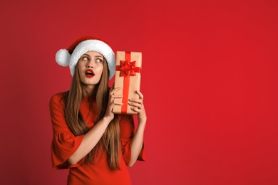 Young beautiful woman in Santa hat with gift box on color background. Christmas celebration