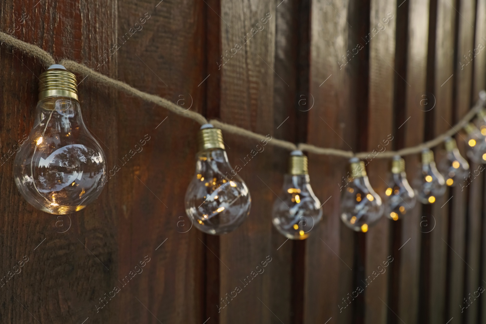 Photo of Garland of lamp bulbs hanging on wooden wall. String lights