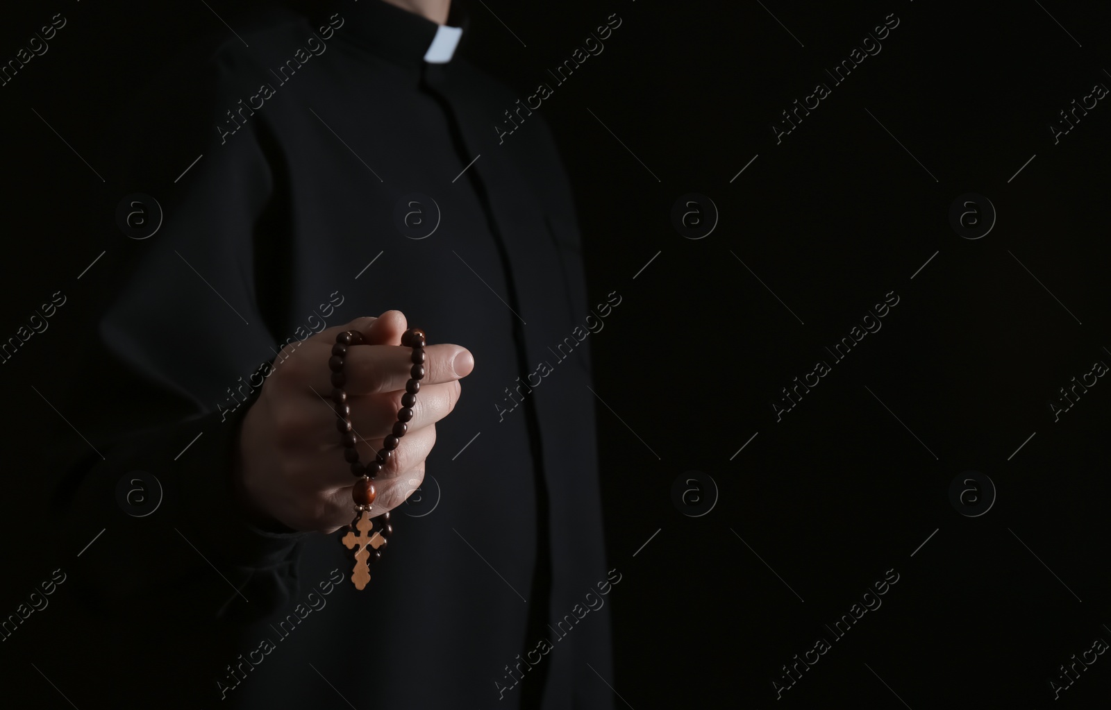 Photo of Priest with rosary beads on dark background, closeup. Space for text