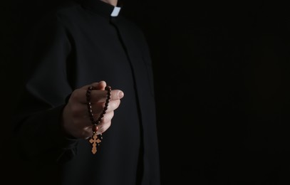 Photo of Priest with rosary beads on dark background, closeup. Space for text