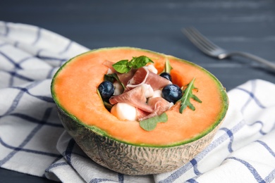 Photo of Half of melon with prosciutto, blueberries and herbs on table