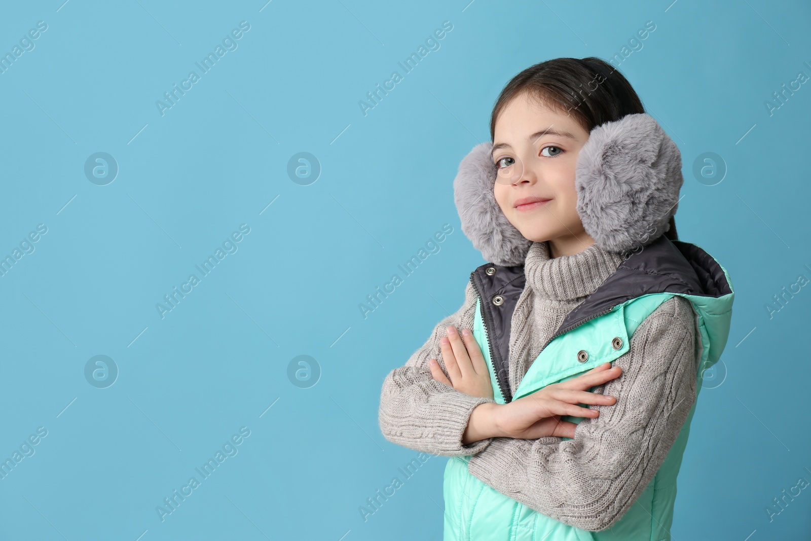 Photo of Cute little girl wearing stylish earmuffs on light blue background. Space for text